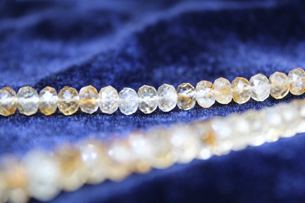 A strand of faceted citrine beads with a blurred strand of pearls in the foreground on a blue velvet background.