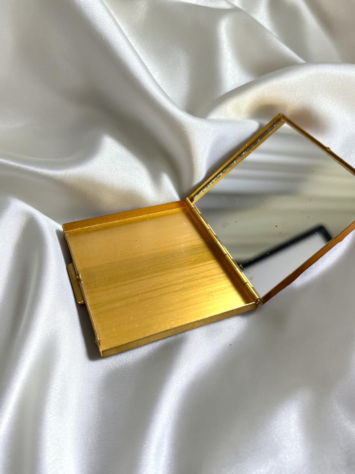 S.F. Co. Fifth Avenue gold tone powder compact with a mirror, open on white satin.