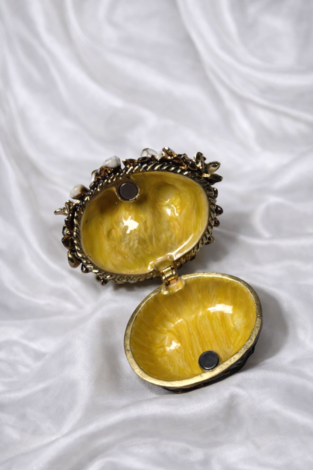 Open yellow enamel trinket box with gold trim and magnetic closure, resting on white satin.