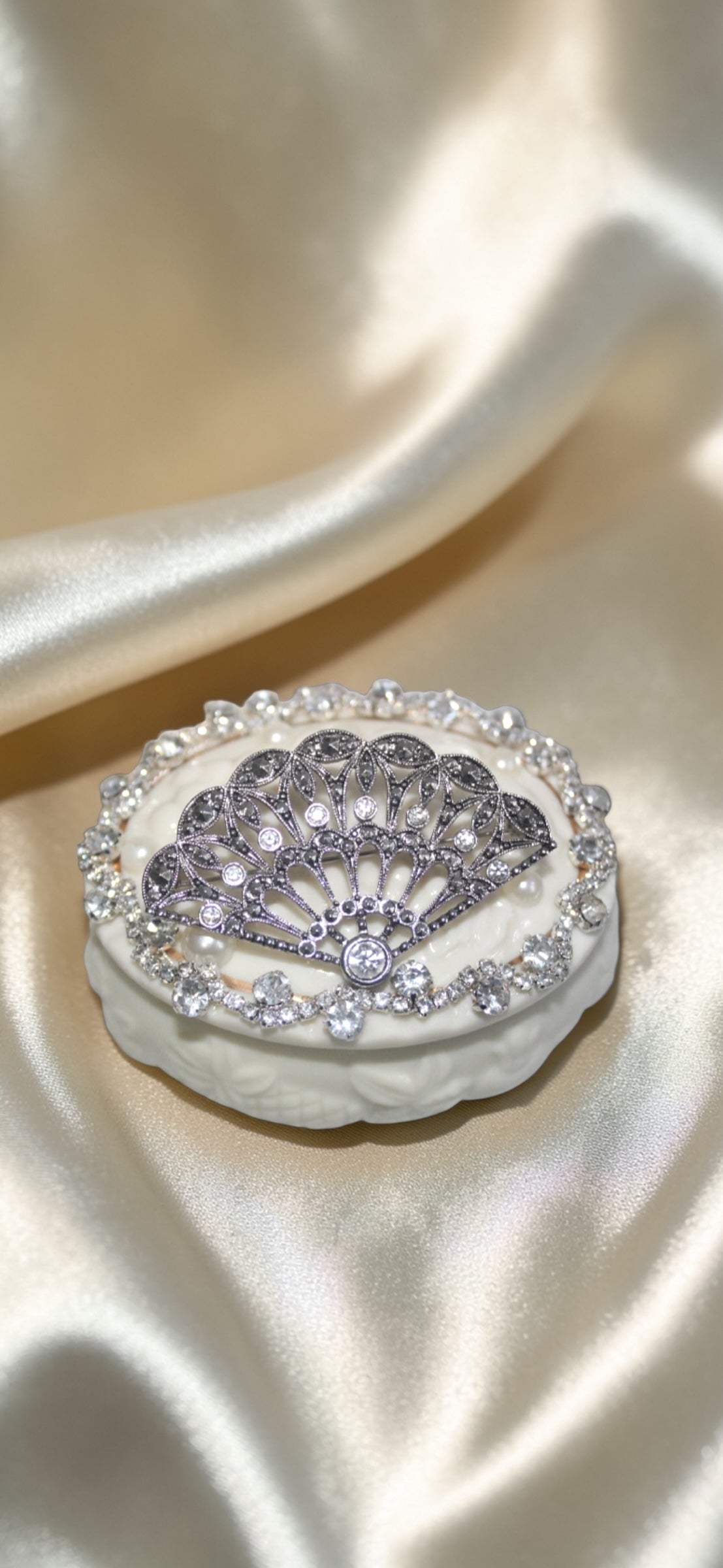 Vintage fan brooch with intricate metalwork and sparkling jewel accents on a white decorative box.
