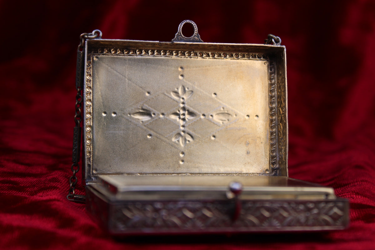 An antique French silver and brass vanity case with an engraved interior on a red background.