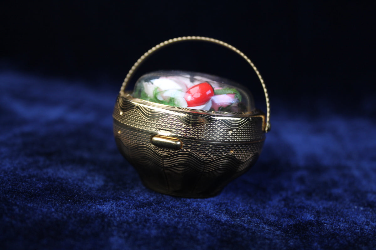 1940s gold-tone compact in a basket design with preserved floral details under a clear dome.