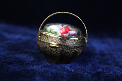 1940s gold-tone compact in a basket design with preserved floral details under a clear dome.