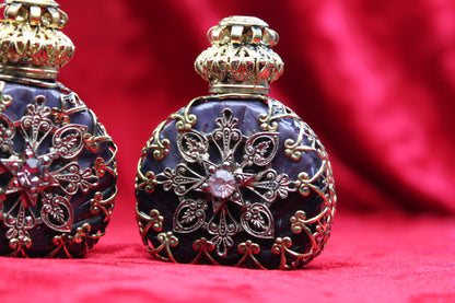 Matched pair of amethyst glass perfume bottles with gold filigree and rhinestone details on a red background.