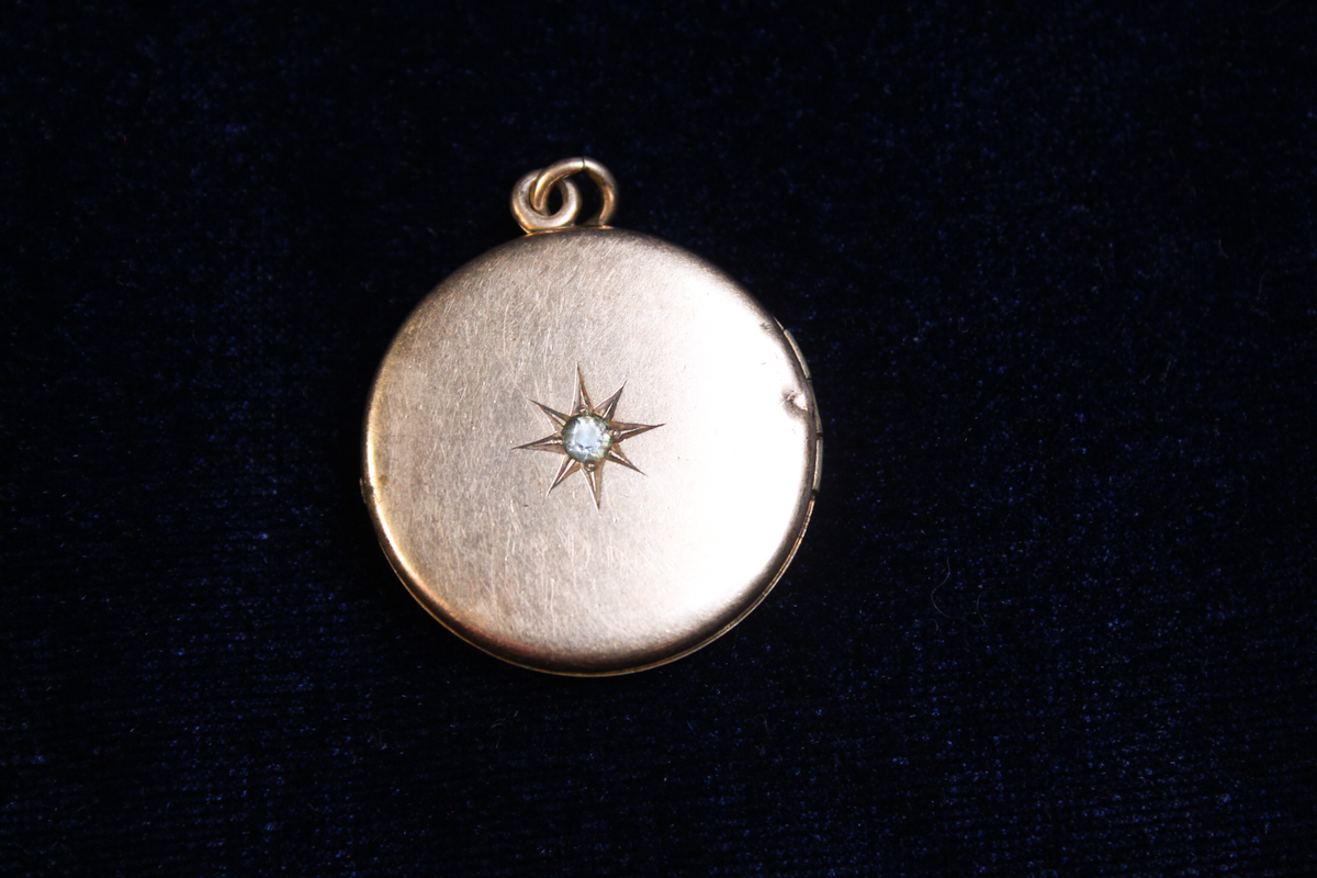 Gold plated locket with a starburst design and a central stone, on a dark background.