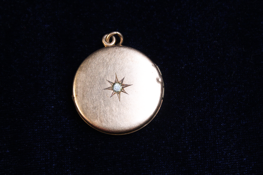 Gold plated locket with a starburst design and a central stone, on a dark background.