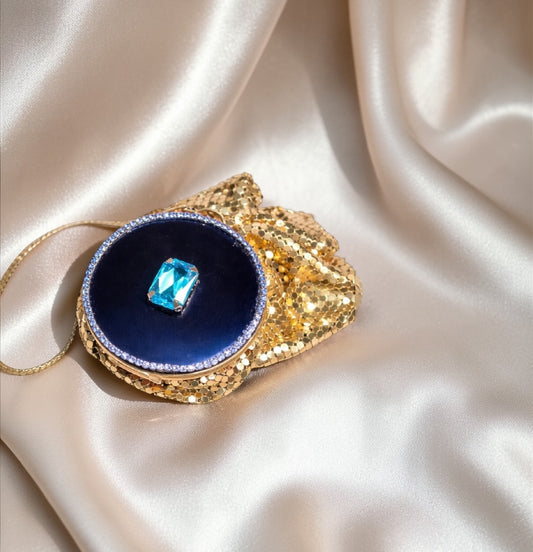 Gold mesh purse compact with a dark blue center, accented by blue crystals and a large blue gem.