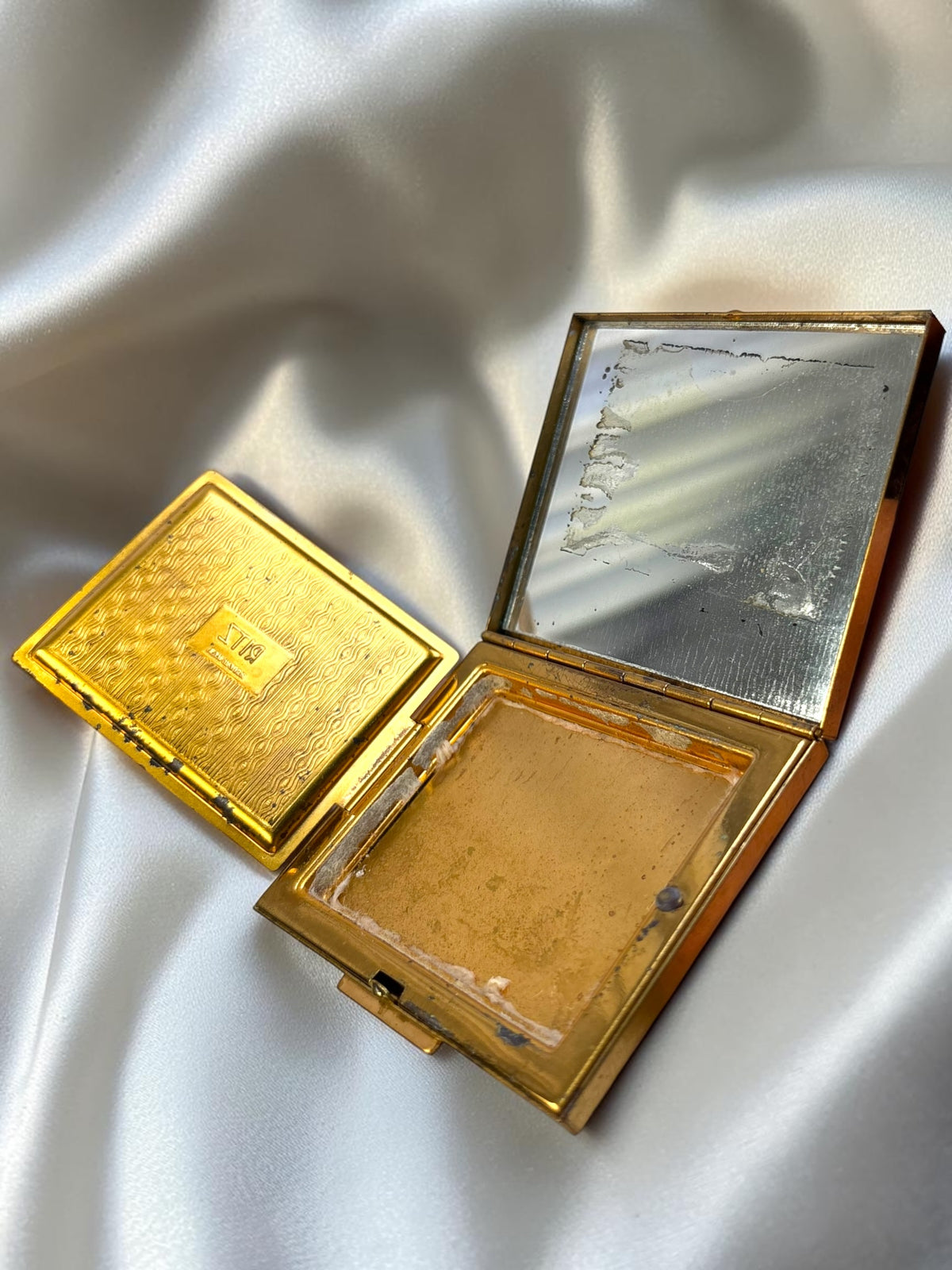 Vintage Ritz gold tone powder compact with rhinestone flower detail, open to show mirror and powder compartment.