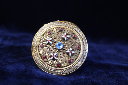 1920s ornate gold-tone filigree mesh purse compact with red and blue glass accents.