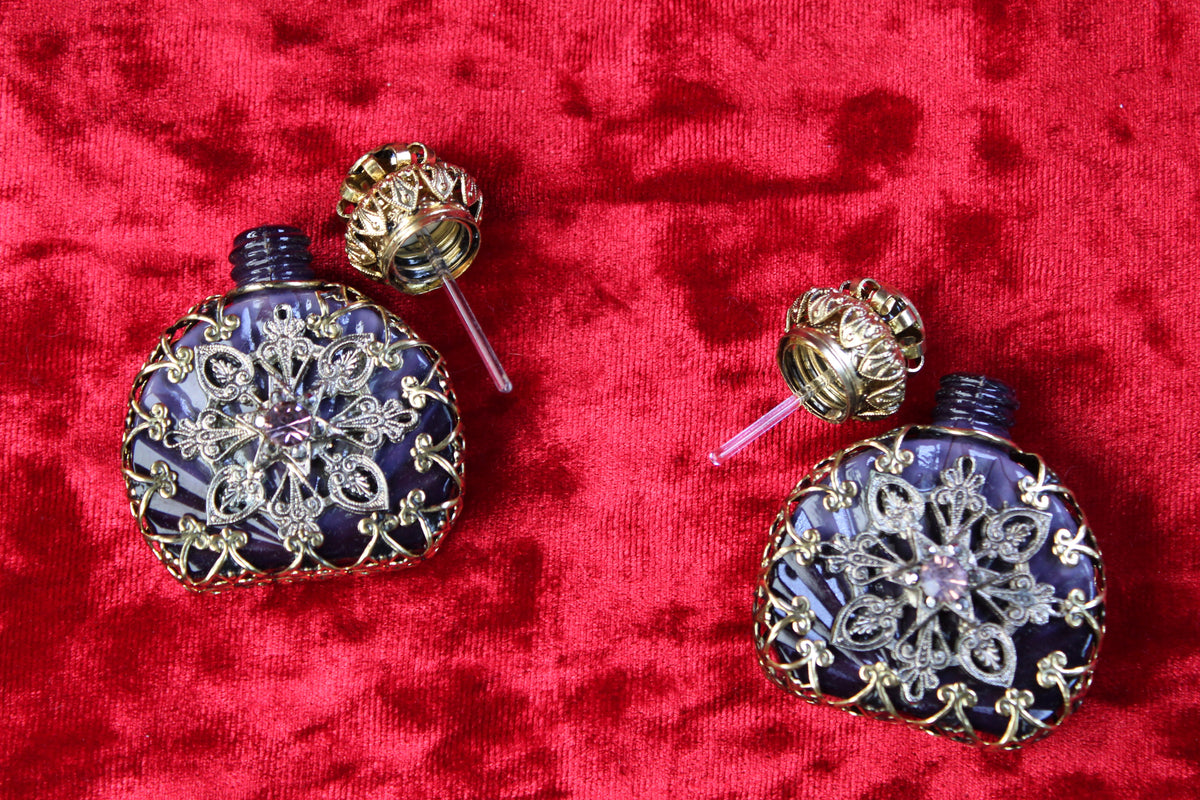 Matched pair of amethyst glass perfume bottles with gold filigree and rhinestone details on red velvet.