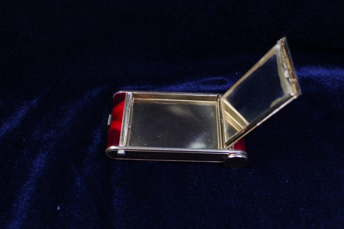 Open vintage gold and red marbled novelty camera compact with mirror and cigarette holder.