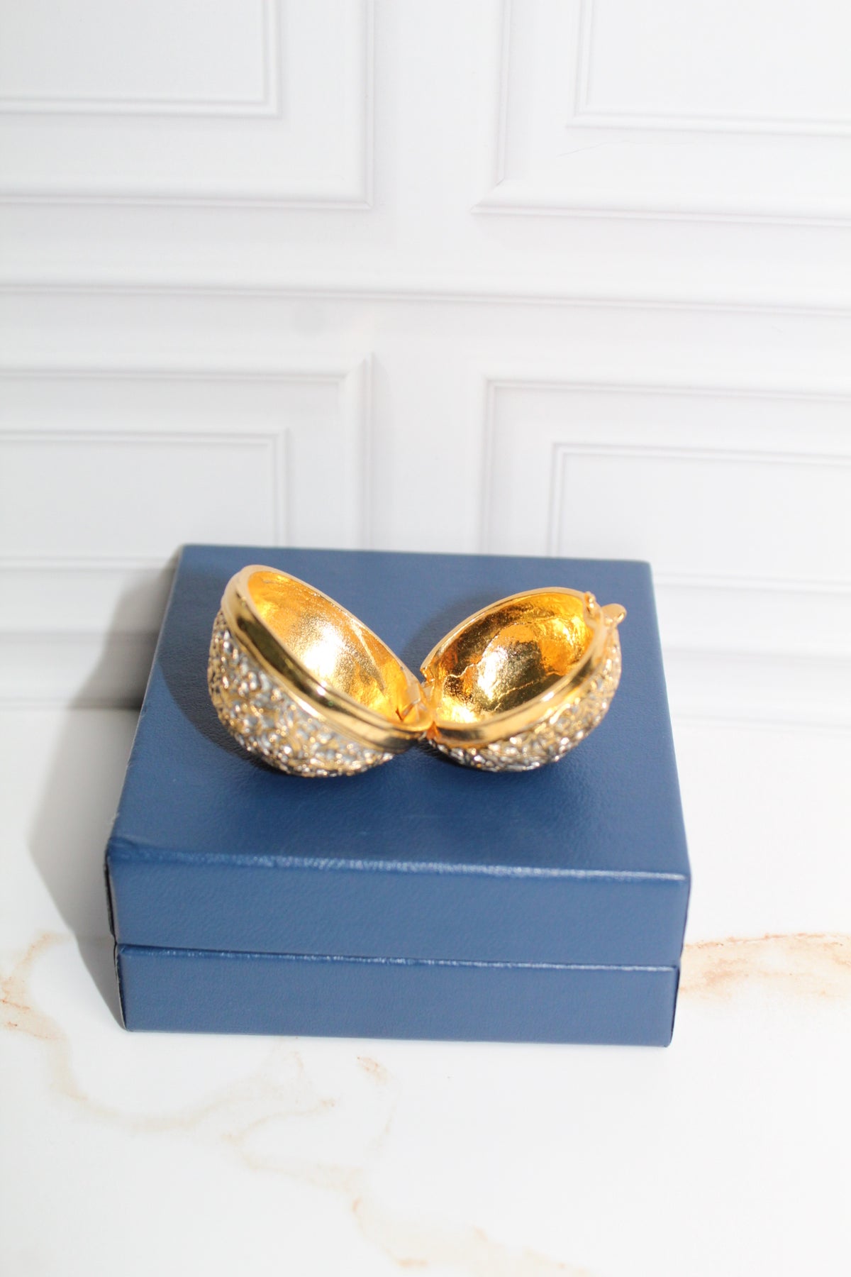Jaestial Gilded Lace Round Trinket Box in vintage gold filigree, open on a blue box.