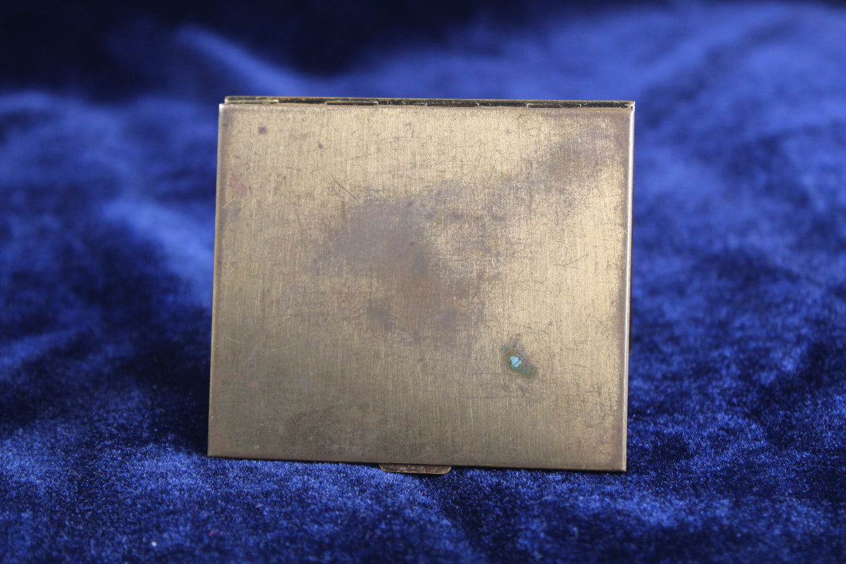 Vintage 1940s gold-tone compact with a weathered surface, resting on a blue velvet cloth.