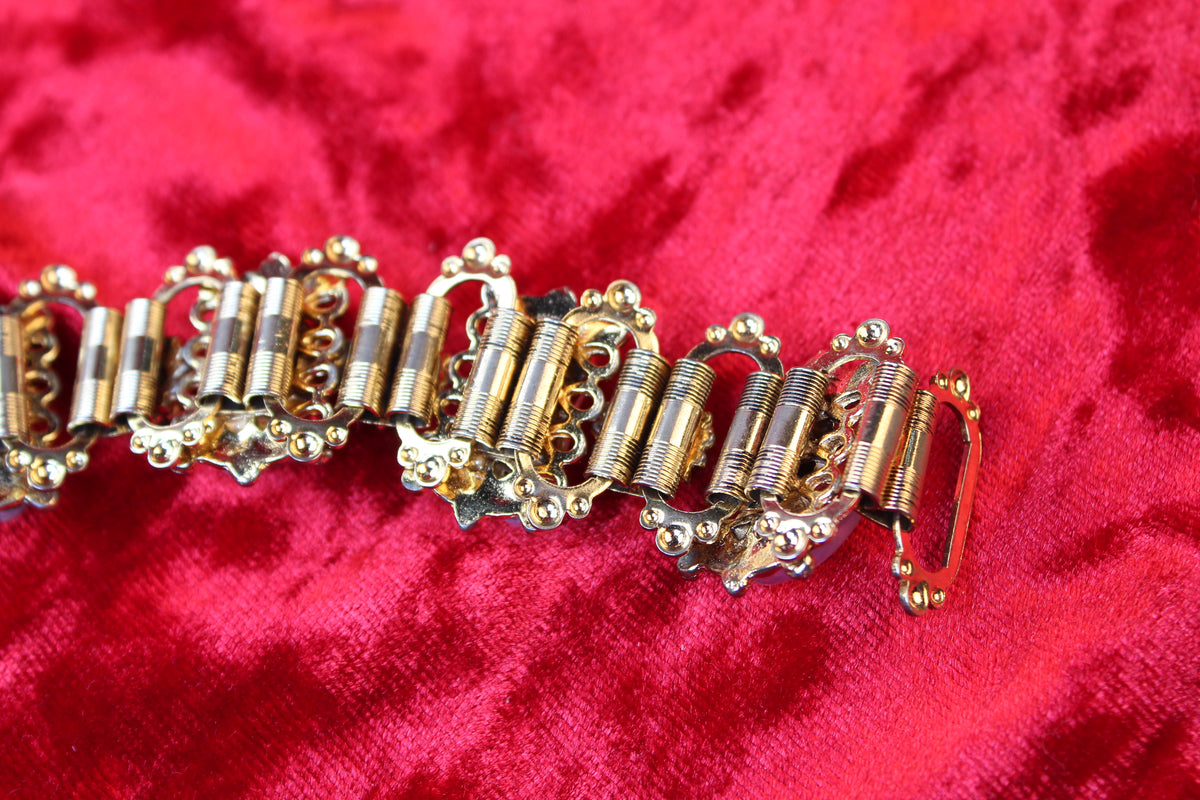 Gold tone bracelet with opalescent glass and garnet rhinestones on red velvet.