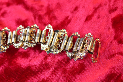 Gold tone bracelet with opalescent glass and garnet rhinestones on red velvet.
