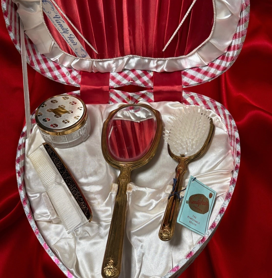 Heart-shaped vanity set with mirror, brush, comb, and powder jar in a red and white plaid case.