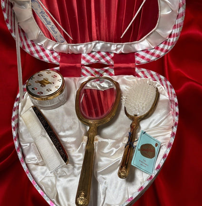 Heart-shaped vanity set with mirror, brush, comb, and powder jar in a red and white plaid case.