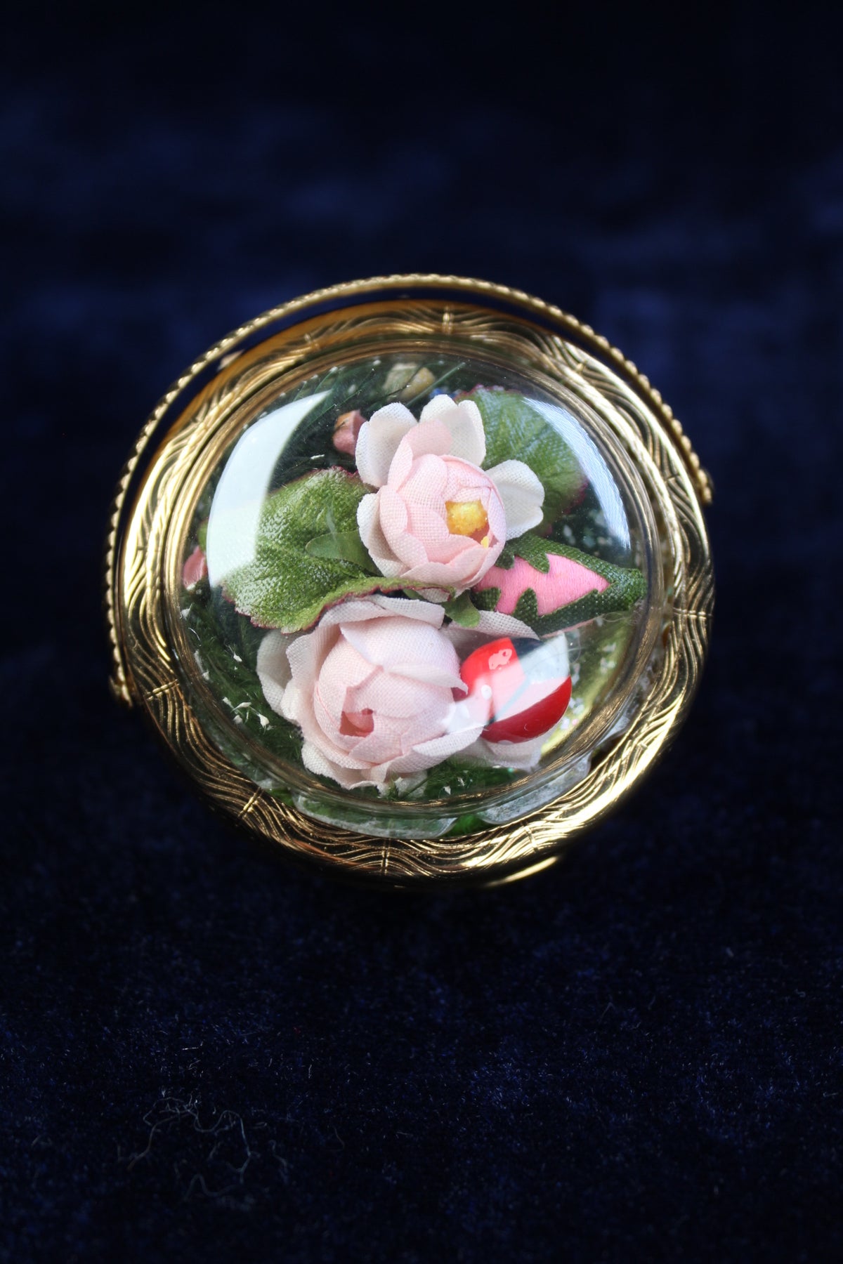 1940s gold-tone compact with preserved pink flowers under a glass dome.