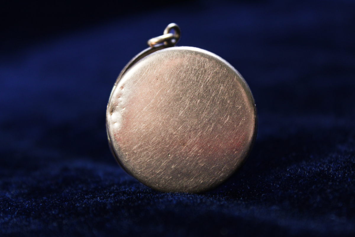 Round gold-plated locket with a starburst design and a broken clasp.