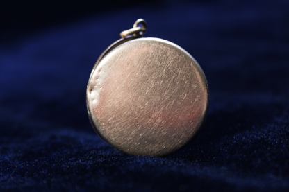 Round gold-plated locket with a starburst design and a broken clasp.