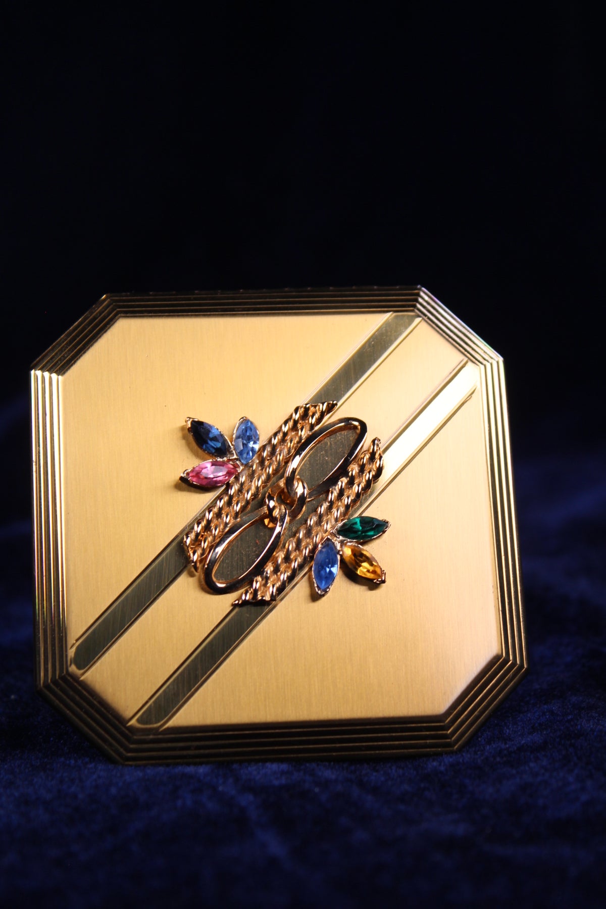 1950s Volupte octagonal gold-tone compact with a rhinestone clasp in jewel tones.