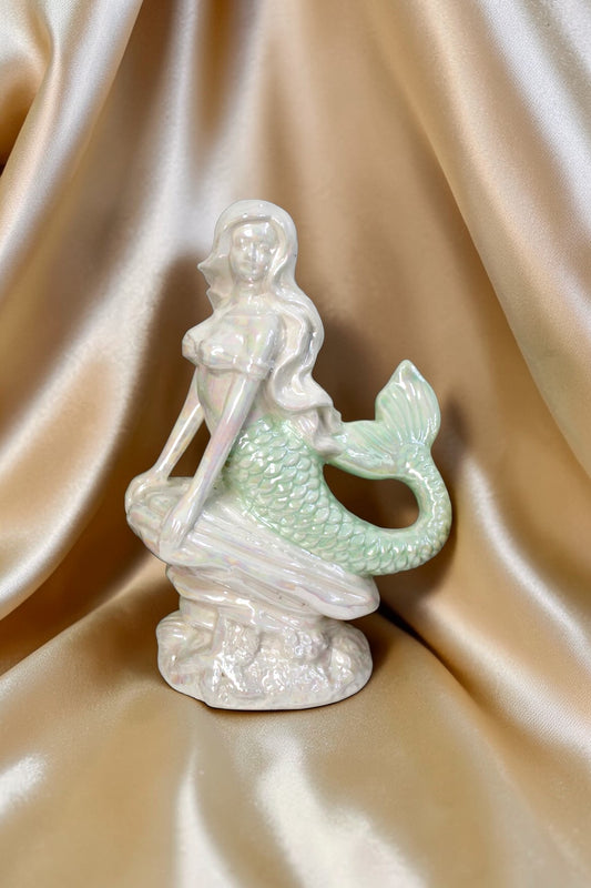 Iridescent ceramic mermaid figurine with pearlescent seafoam and ivory tones, sitting on a rock.