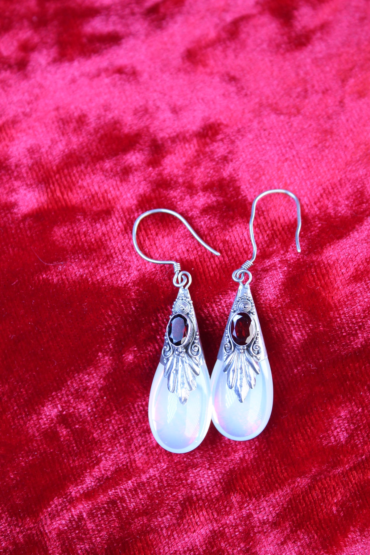 Sterling silver dangle earrings with red garnets and opalite teardrops on a red velvet background.