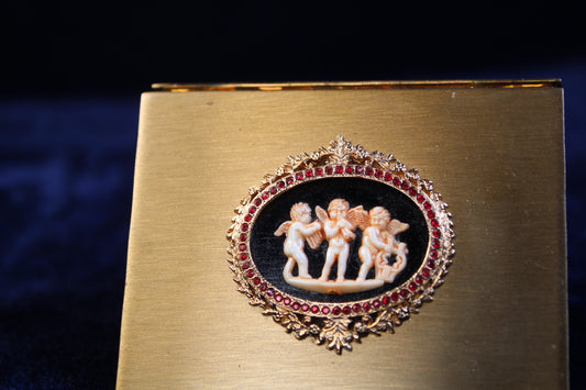 1940s Volupte compact with gold-tone finish, featuring a cherub cameo and ruby rhinestones.