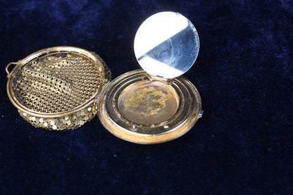 Ornate gold-tone filigree mesh purse compact case with an open lid revealing a mirror and compartment.