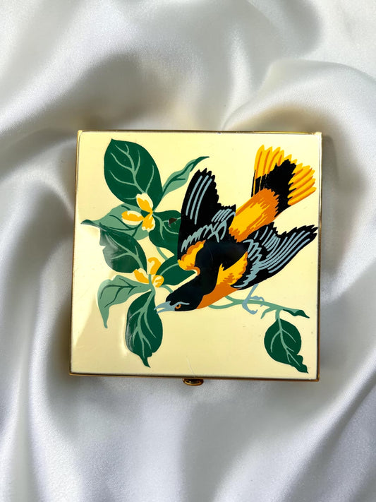 Vintage Wadsworth powder compact with a gold-tone finish, featuring a colorful bird on a branch with green leaves and yellow flowers.