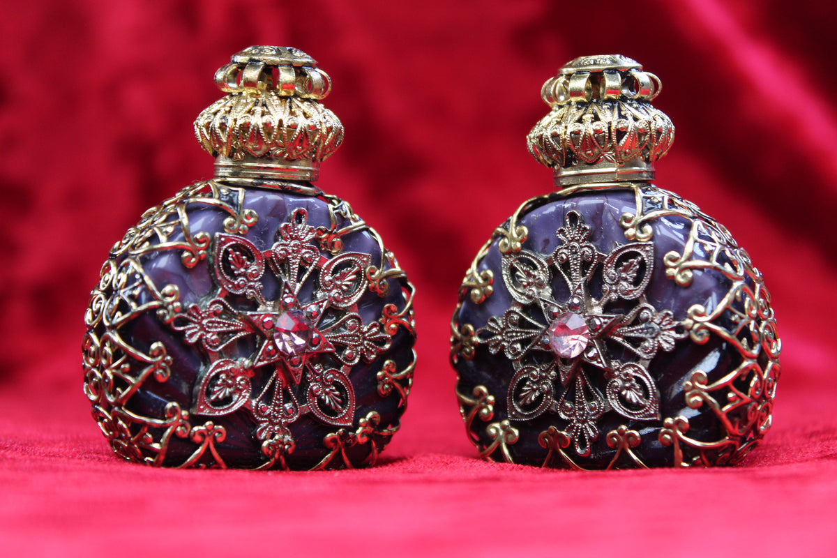 Matched pair of amethyst glass perfume bottles with gold-tone filigree and rhinestone accents.