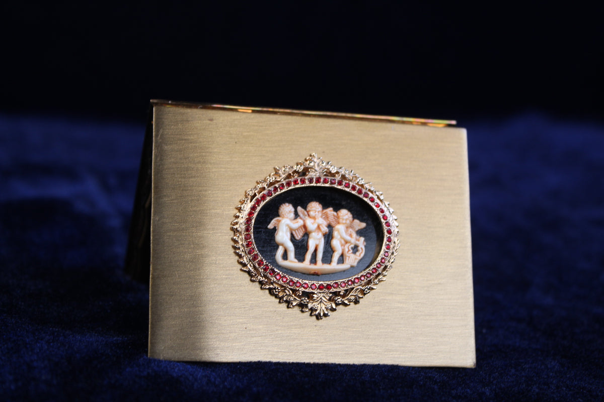 1940s Volupte compact with gold-tone finish, featuring a cherub cameo and ruby rhinestones.