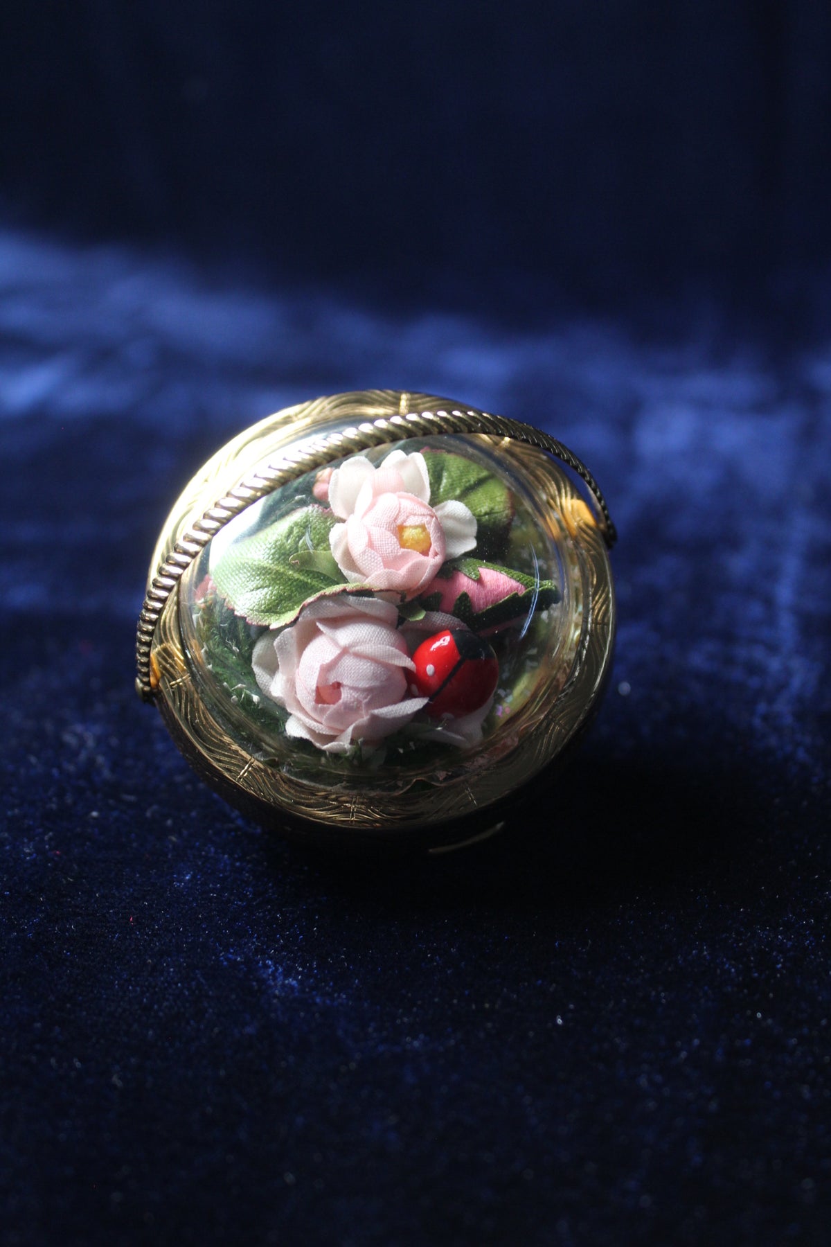 Gold-tone compact with a clear dome showcasing preserved pink roses and a ladybug.