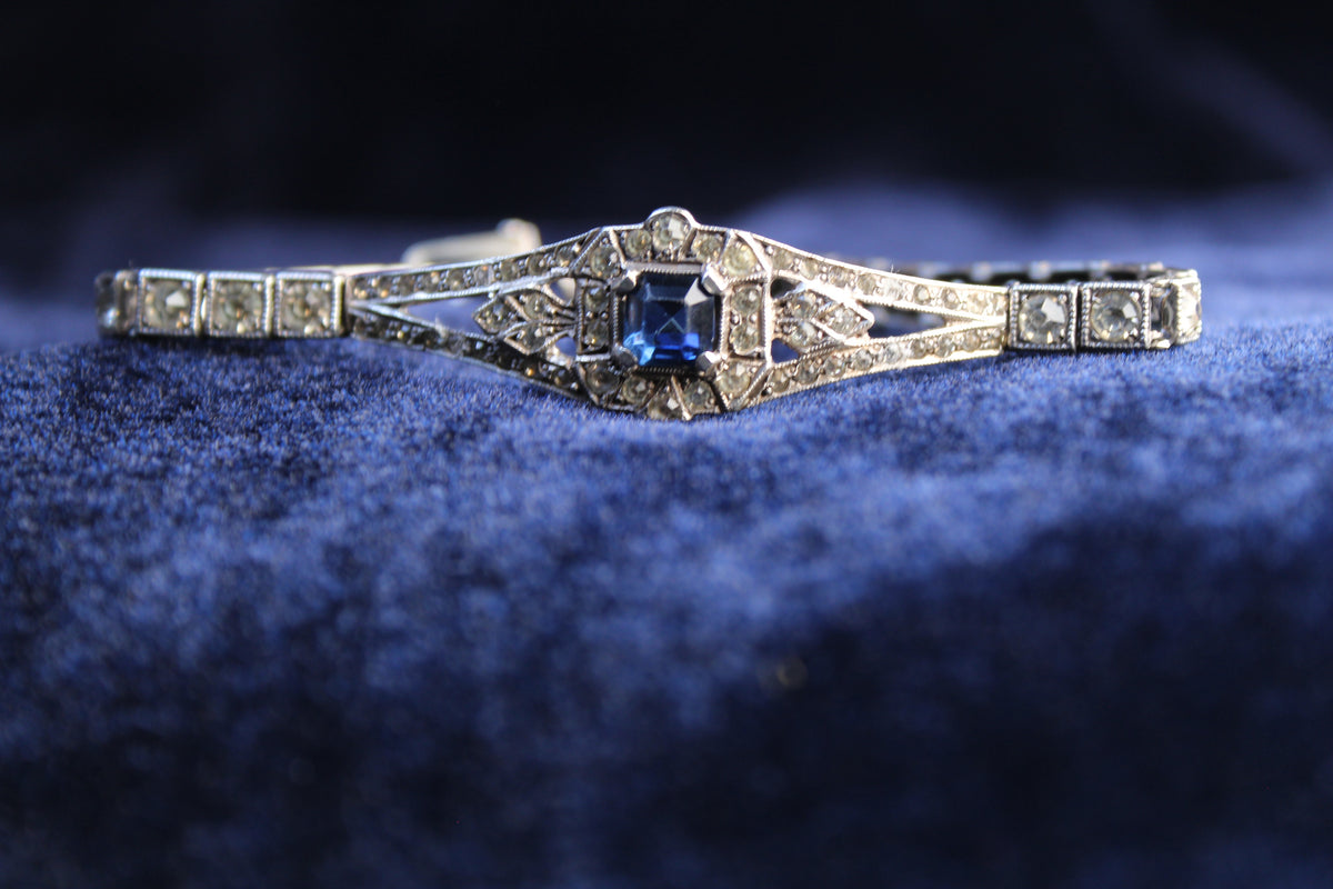 Sterling silver Art Deco bracelet with a central sapphire-blue paste stone and surrounding clear paste stones.