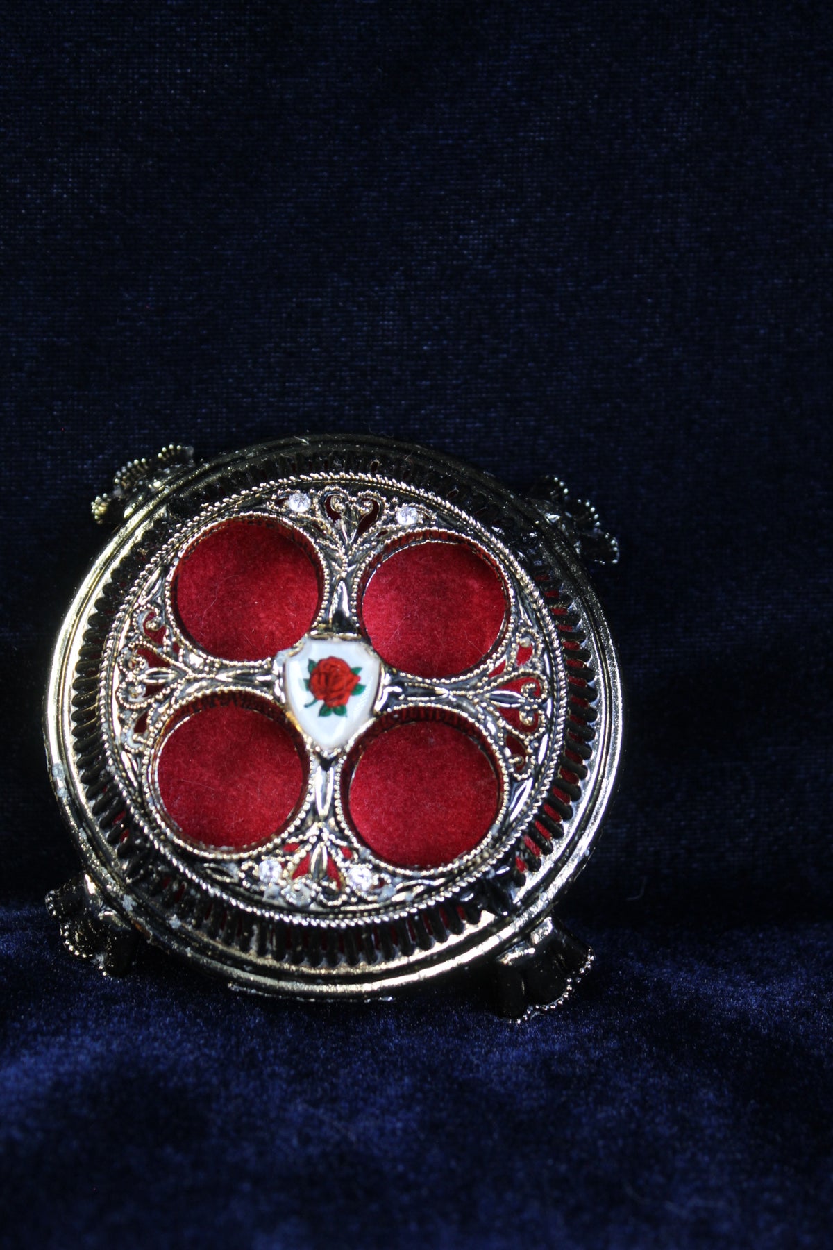 Vintage lipstick holder with red velvet interior and an enchanted rose emblem.