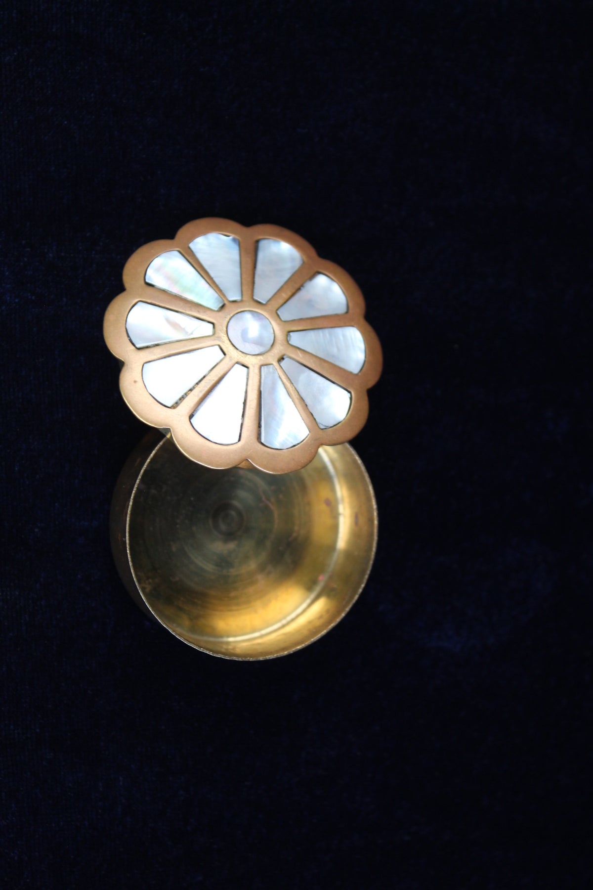 Brass ring box with a floral mother-of-pearl inlay lid, set against a dark blue velvet background.
