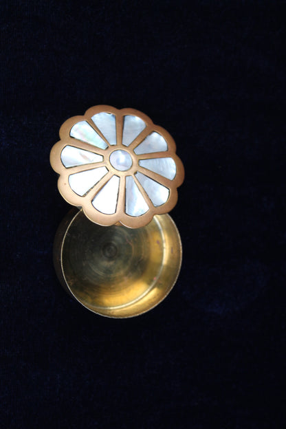 Brass ring box with a floral mother-of-pearl inlay lid, set against a dark blue velvet background.