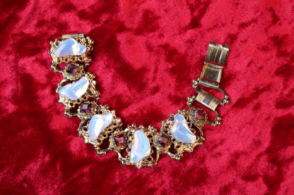Gold tone bracelet with opalescent glass and garnet rhinestones on red velvet