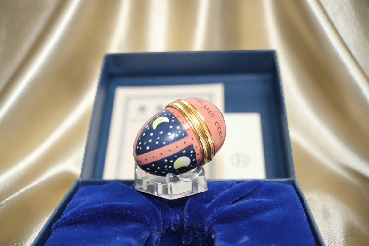 Halcyon Days navy egg trinket box with moon and stars design, resting in a blue velvet-lined box.