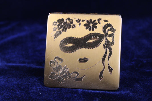 1940s gold tone vanity compact with engraved masquerade mask and floral motif.