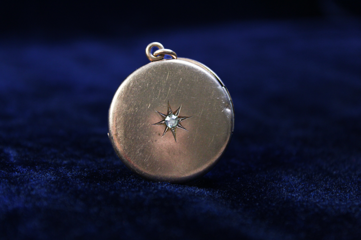 Antique gold plated locket with a starburst design and a central stone, on a dark blue velvet background.