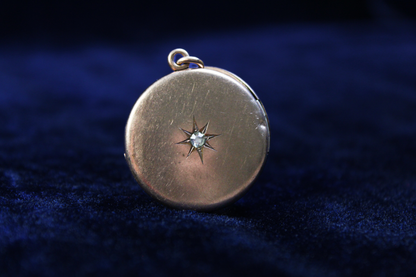 Antique gold plated locket with a starburst design and a central stone, on a dark blue velvet background.