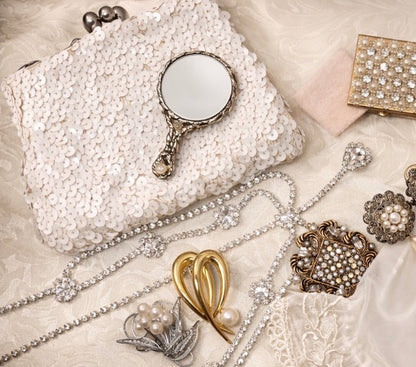 White sequin clutch with a vintage hand mirror, diamond necklaces, and brooches.
