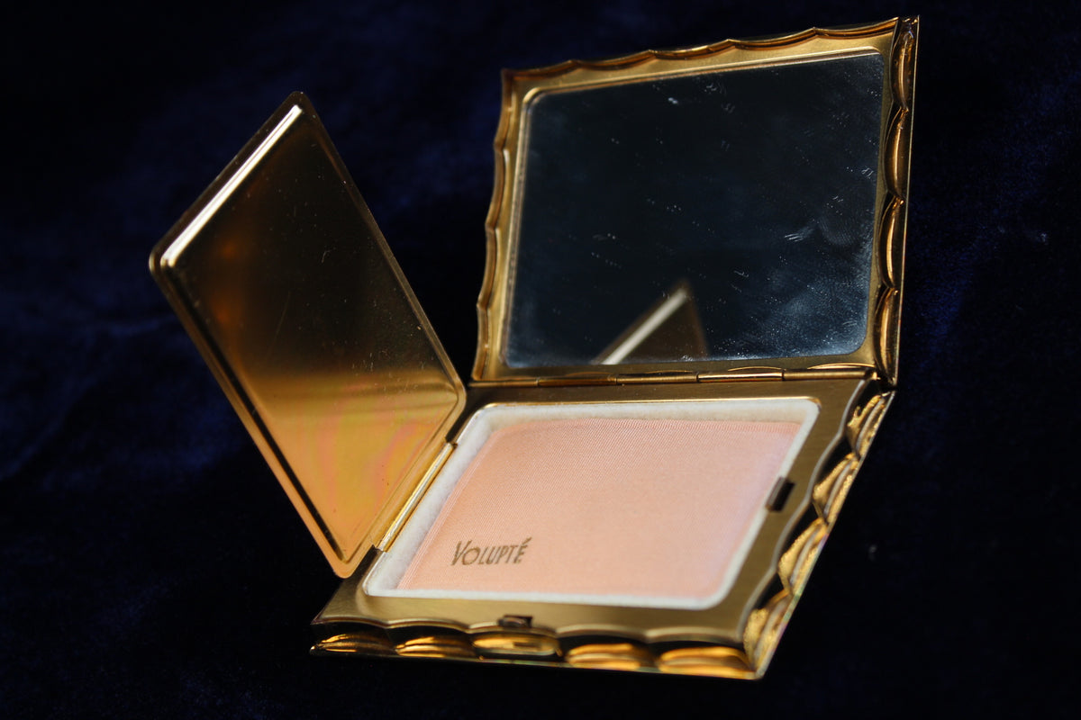 Gold-tone Volupte compact open to show powder and mirror. The powder has "VOLUPTÉ" imprinted on it.