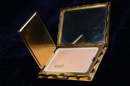 Gold-tone Volupte compact open to show powder and mirror. The powder has "VOLUPTÉ" imprinted on it.
