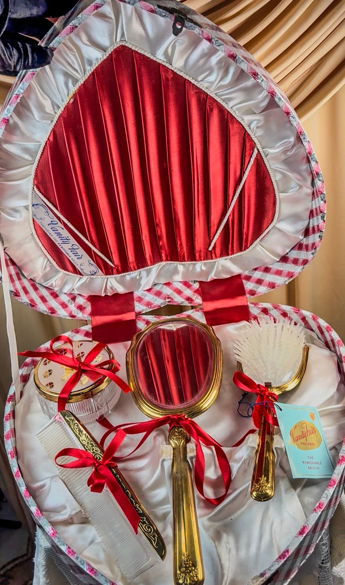 Heart-shaped vanity set with red satin lining, featuring a gilt mirror, hairbrush, comb, and powder jar.