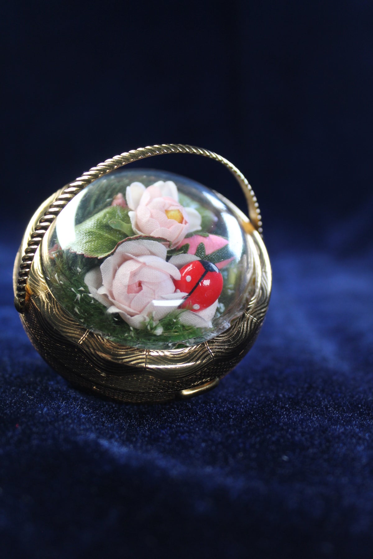 Gold-tone basket compact with a clear dome showcasing pink roses, greenery, and a ladybug.