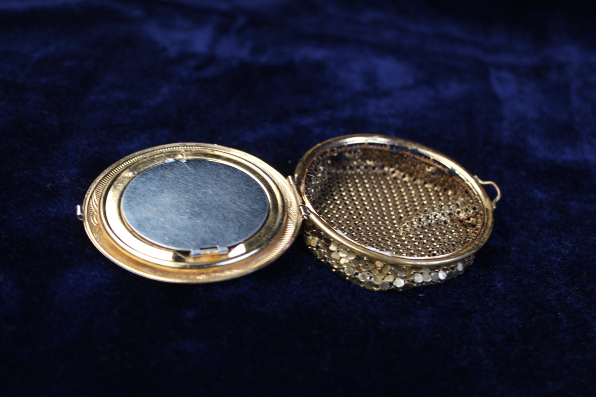 Ornate gold-tone 1920s filigree mesh purse compact case with red and blue glass accents, open.