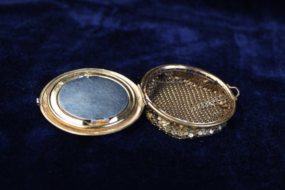 Ornate gold-tone 1920s filigree mesh purse compact case with red and blue glass accents, open.