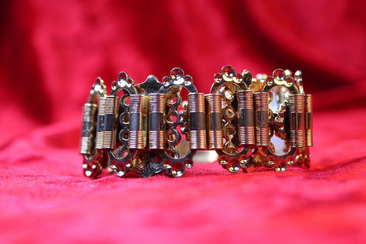 Gold tone bracelet with opalescent glass and garnet rhinestones on a red velvet background.